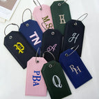 Embroidered leather-look bag tags with gold, white and blue monogram stitching