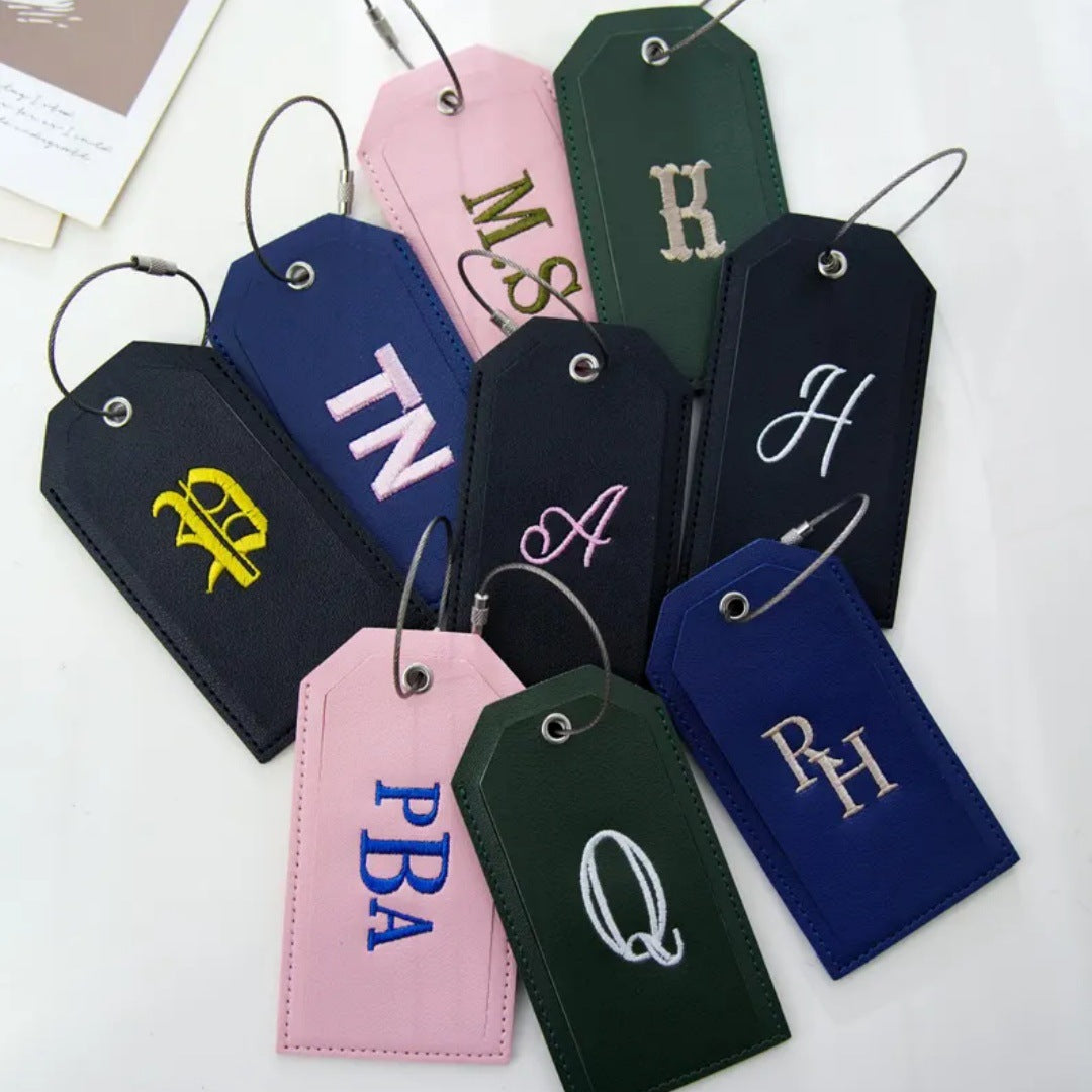 Embroidered leather-look bag tags with gold, white and blue monogram stitching