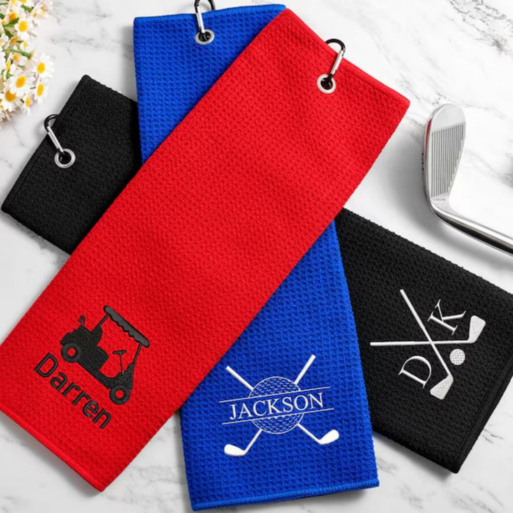 Personalized golf towels embroidered with Darren, Jackson and DK initials beside a golf club