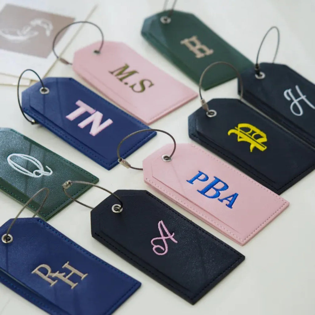 Personalized luggage tags embroidered with initials like MS, TN and PBA in pink, navy, green and black