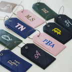 Personalized luggage tags embroidered with initials like MS, TN and PBA in pink, navy, green and black