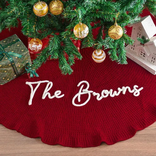 Personalized Christmas tree skirt in red knit with The Browns embroidered in white script under a decorated tree