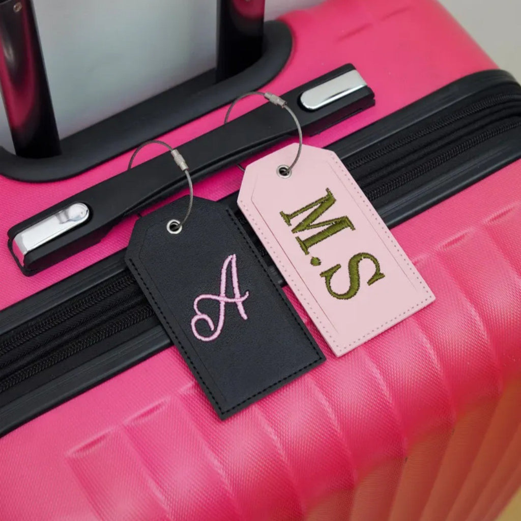 Black and pink name tags with A and M.S initials hanging from a pink suitcase handle
